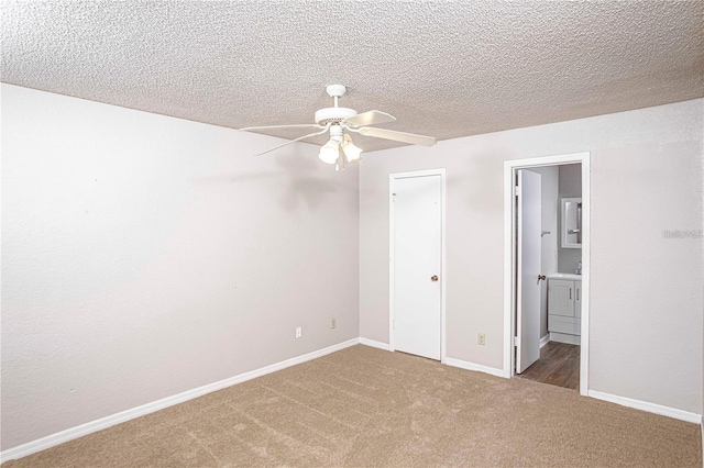 unfurnished bedroom with ceiling fan, a textured ceiling, connected bathroom, and dark colored carpet