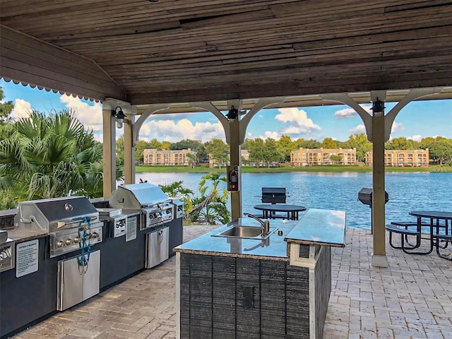 view of patio with a water view, an outdoor kitchen, a grill, and sink