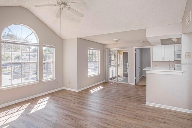 unfurnished living room featuring ceiling fan, light hardwood / wood-style flooring, plenty of natural light, and lofted ceiling