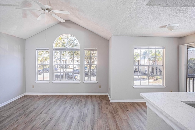 unfurnished dining area featuring ceiling fan, vaulted ceiling, a textured ceiling, and light hardwood / wood-style floors