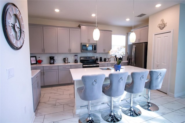 kitchen with sink, stainless steel appliances, decorative light fixtures, a kitchen island with sink, and a breakfast bar