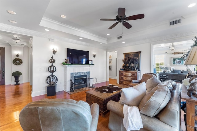 living room with a tray ceiling, ceiling fan with notable chandelier, a fireplace, hardwood / wood-style floors, and crown molding