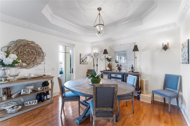 dining room with wood-type flooring, a tray ceiling, and crown molding