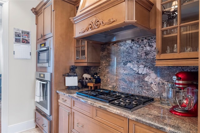 kitchen featuring black gas stovetop, custom range hood, stainless steel oven, and decorative backsplash