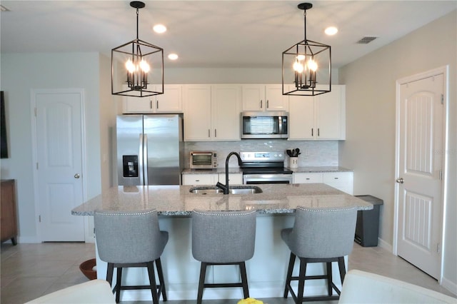 kitchen with an island with sink, pendant lighting, stainless steel appliances, and white cabinets