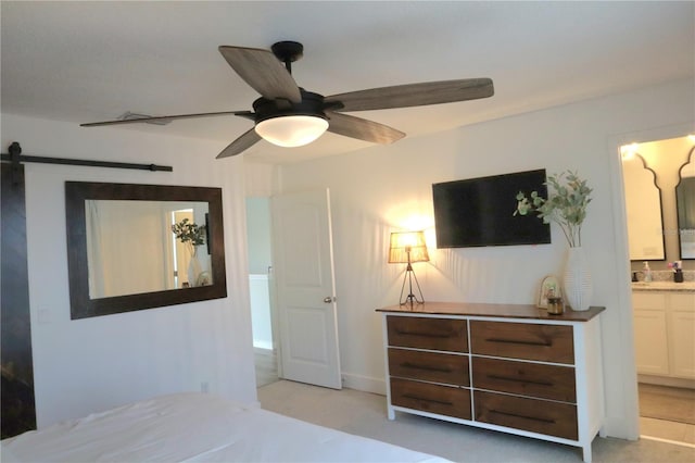 bedroom with light carpet, ensuite bath, ceiling fan, and a barn door