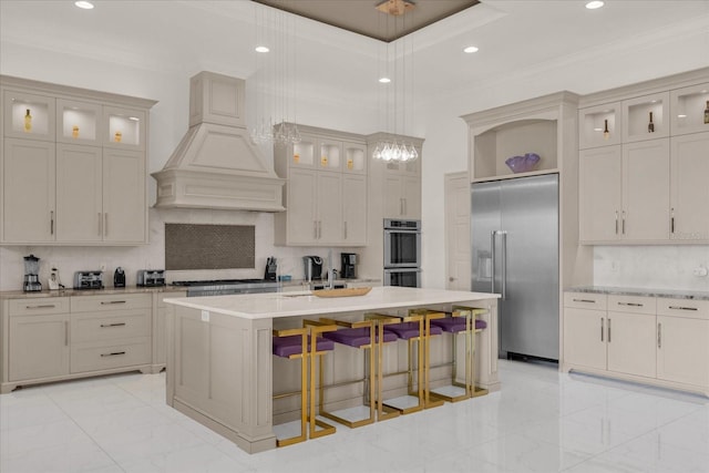 kitchen with pendant lighting, premium range hood, a kitchen island with sink, stainless steel appliances, and crown molding