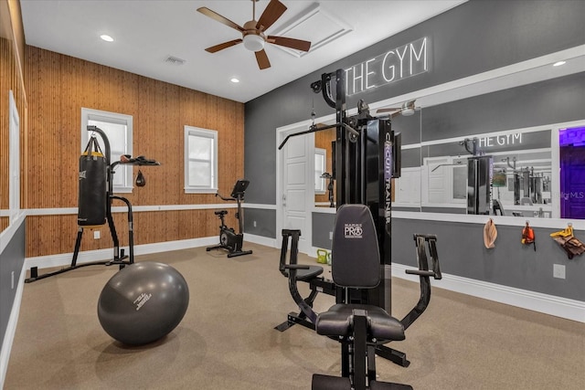 workout room with ceiling fan, light colored carpet, and wooden walls