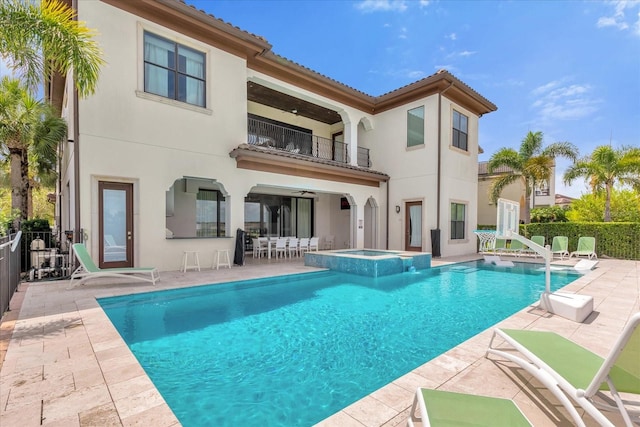 back of property featuring a balcony, a patio, and a swimming pool with hot tub