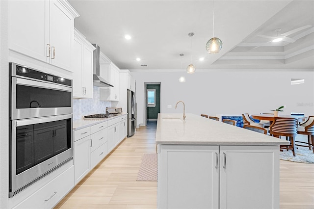 kitchen with a kitchen island with sink, pendant lighting, stainless steel appliances, and white cabinetry