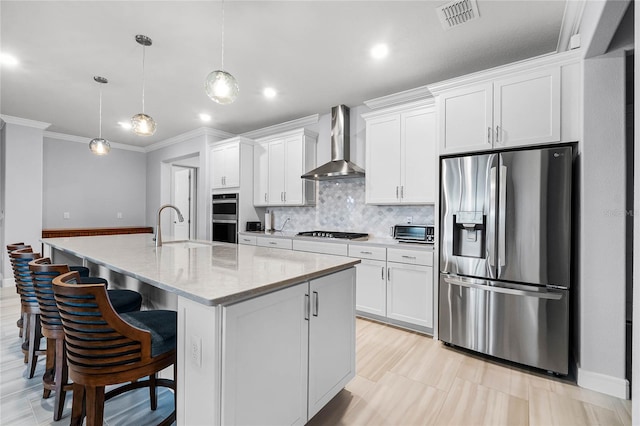 kitchen with pendant lighting, a kitchen island with sink, appliances with stainless steel finishes, and wall chimney range hood