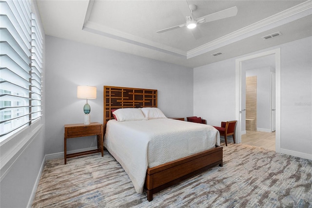 bedroom with light wood-type flooring, a tray ceiling, connected bathroom, crown molding, and ceiling fan