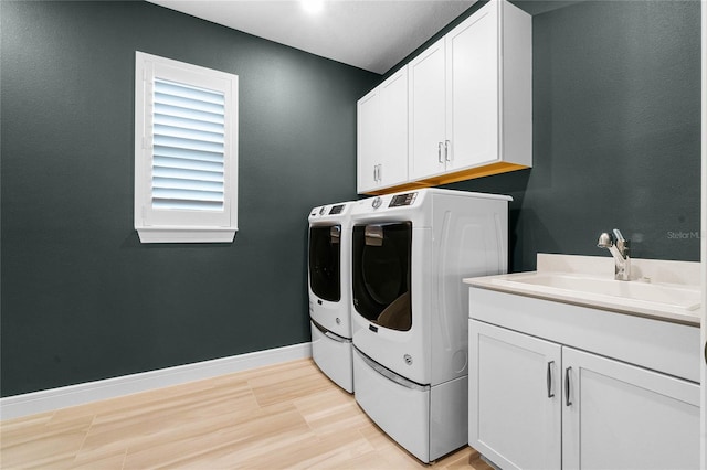 clothes washing area featuring cabinets, light hardwood / wood-style floors, washer and dryer, and sink