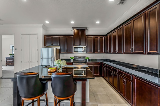 kitchen featuring light tile patterned floors, dark brown cabinets, a center island with sink, appliances with stainless steel finishes, and crown molding