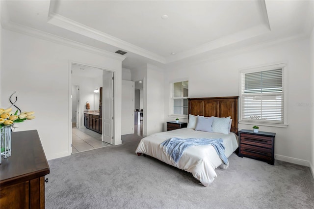 carpeted bedroom with ornamental molding, ensuite bath, and a tray ceiling