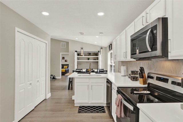 kitchen with white cabinets, lofted ceiling, kitchen peninsula, sink, and appliances with stainless steel finishes