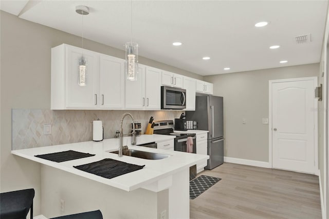 kitchen featuring appliances with stainless steel finishes, hanging light fixtures, kitchen peninsula, and white cabinetry