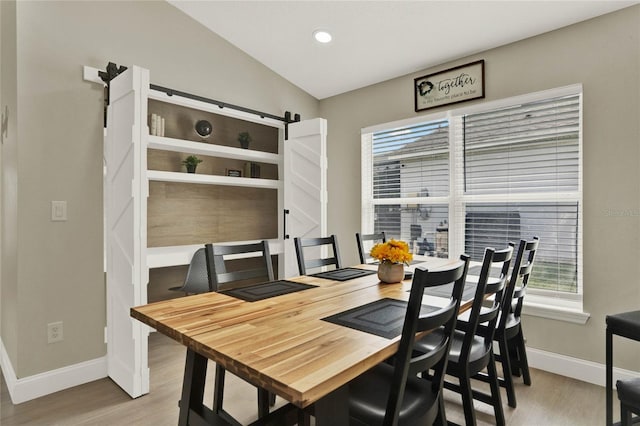 dining space featuring light wood-type flooring, a barn door, and vaulted ceiling