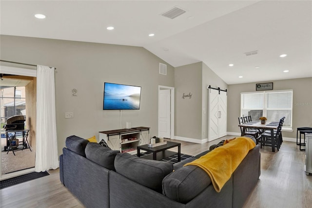 living room featuring a wealth of natural light, vaulted ceiling, wood-type flooring, and a barn door