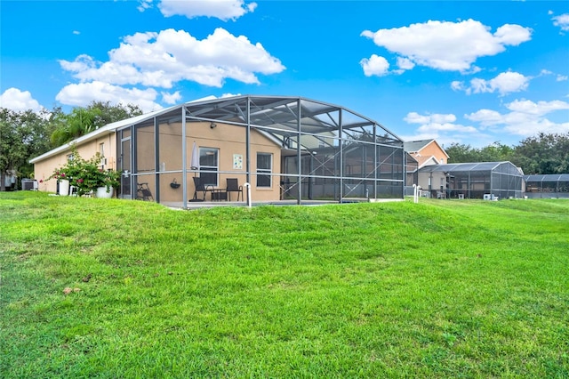 rear view of house with glass enclosure, a patio area, and a lawn