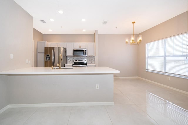 kitchen with appliances with stainless steel finishes, white cabinets, backsplash, light tile patterned floors, and decorative light fixtures