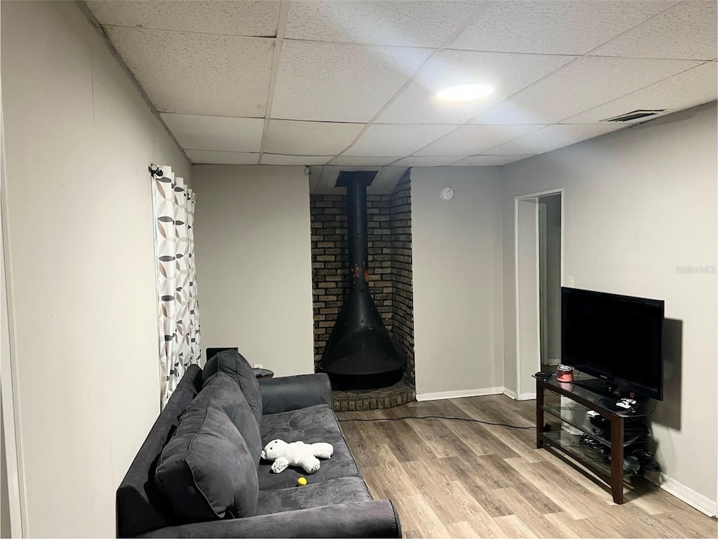 living room featuring wood-type flooring, a drop ceiling, and a wood stove