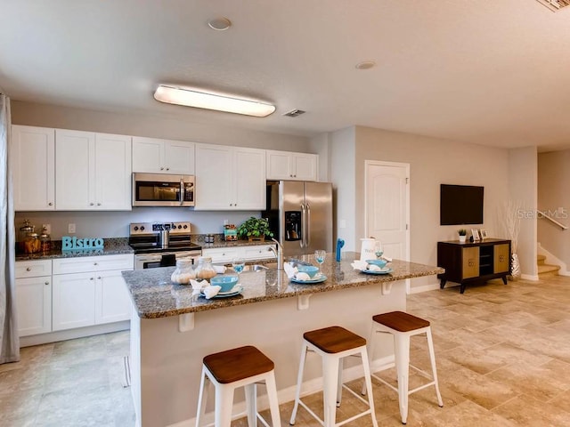 kitchen with appliances with stainless steel finishes, a center island with sink, a breakfast bar, and white cabinets