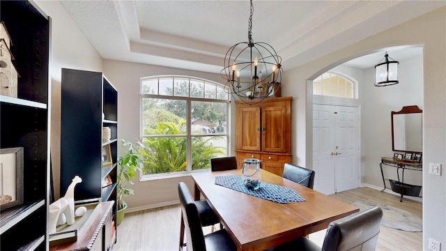 dining area featuring a raised ceiling, a chandelier, and light wood-type flooring