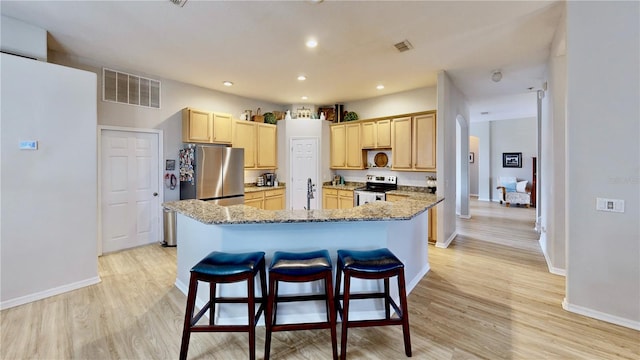 kitchen with light wood-type flooring, light stone counters, a center island, stainless steel appliances, and light brown cabinetry