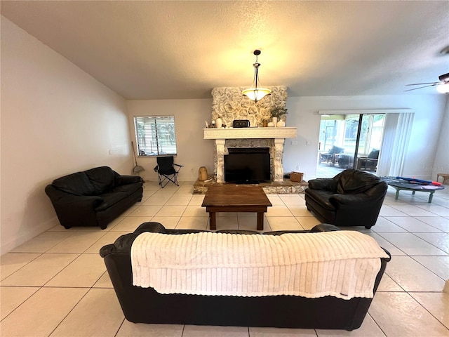 tiled living room with ceiling fan, a textured ceiling, a fireplace, and a wealth of natural light