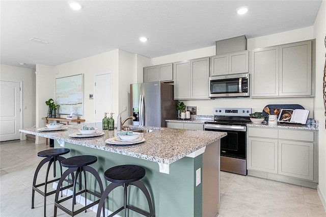 kitchen with gray cabinets, an island with sink, a breakfast bar area, and stainless steel appliances