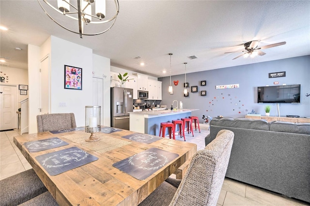 dining area with ceiling fan with notable chandelier, a textured ceiling, sink, and light tile patterned floors