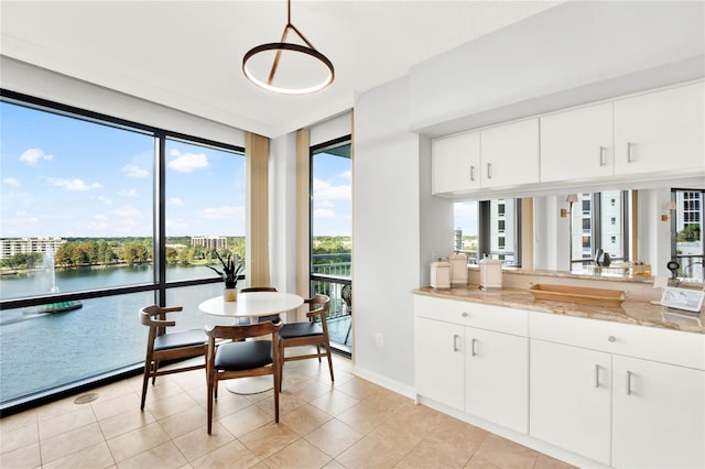 kitchen with pendant lighting, a water view, light stone counters, and white cabinetry