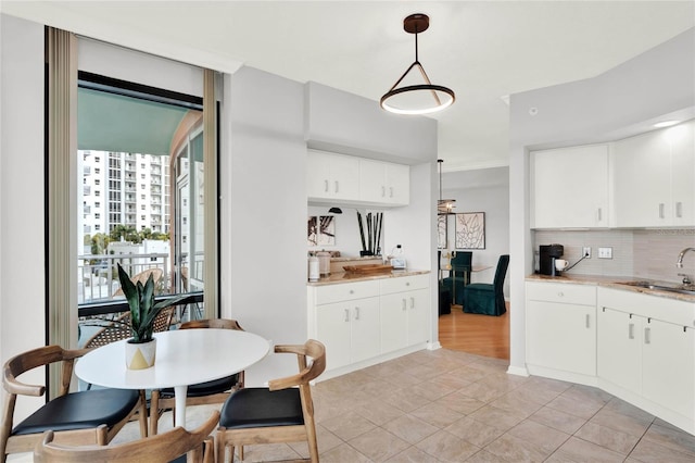 kitchen with a sink, decorative backsplash, hanging light fixtures, and white cabinetry