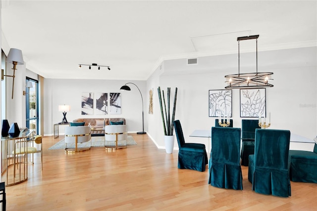 dining space featuring a notable chandelier, light hardwood / wood-style flooring, crown molding, and rail lighting