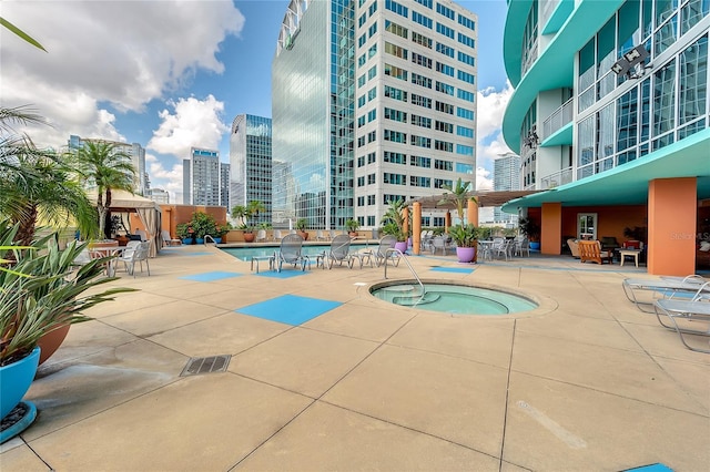 community pool featuring a view of city, a hot tub, and a patio area