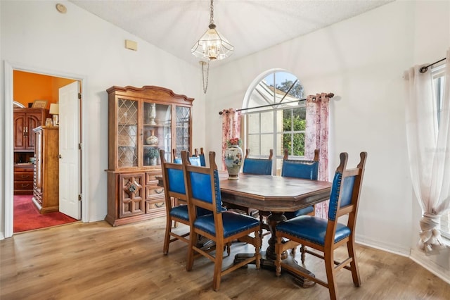 dining area featuring lofted ceiling, a textured ceiling, wood-type flooring, and an inviting chandelier