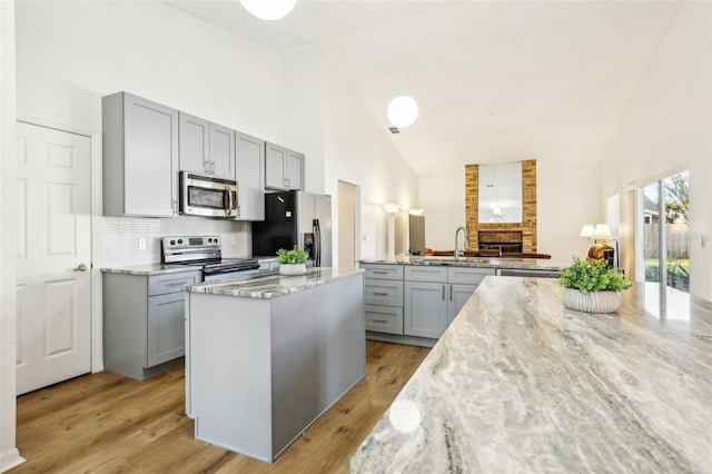 kitchen featuring light hardwood / wood-style floors, stainless steel appliances, sink, light stone countertops, and high vaulted ceiling