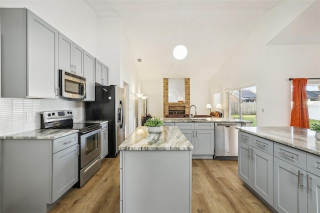 kitchen with a kitchen island, appliances with stainless steel finishes, light stone countertops, light hardwood / wood-style flooring, and gray cabinets