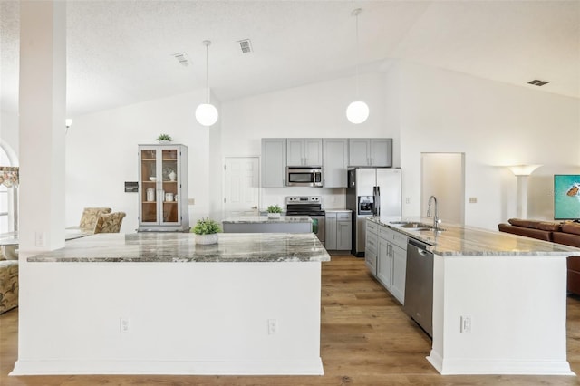 kitchen with appliances with stainless steel finishes, light stone countertops, pendant lighting, gray cabinets, and sink