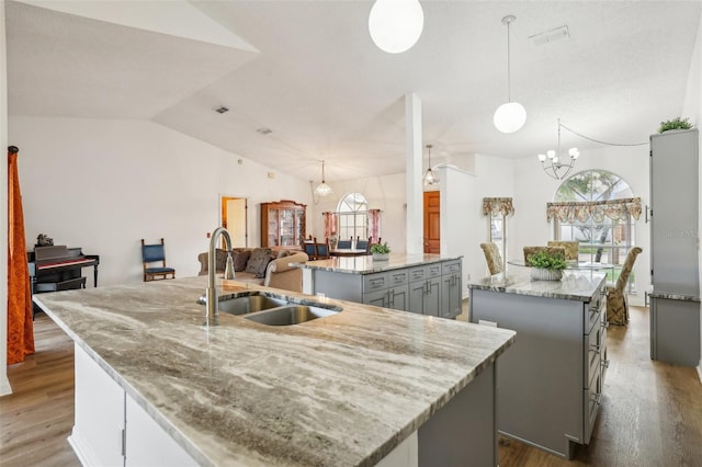 kitchen featuring an inviting chandelier, sink, pendant lighting, and an island with sink