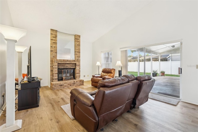 living room featuring decorative columns, light hardwood / wood-style flooring, a brick fireplace, and high vaulted ceiling