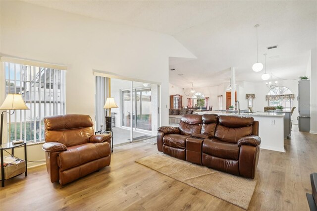 living room featuring light hardwood / wood-style floors, a chandelier, sink, and vaulted ceiling