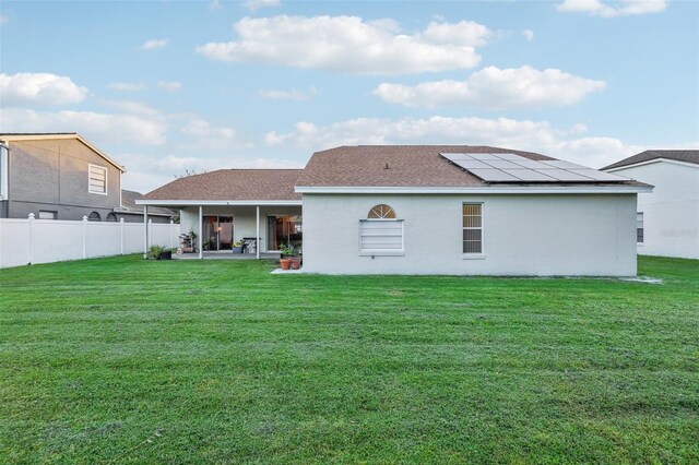 back of house featuring a patio, a yard, and solar panels