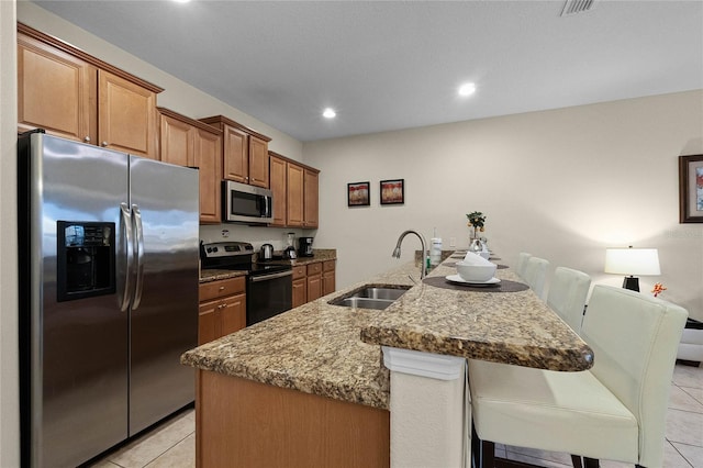 kitchen featuring stainless steel appliances, sink, a center island with sink, a kitchen bar, and light tile patterned floors