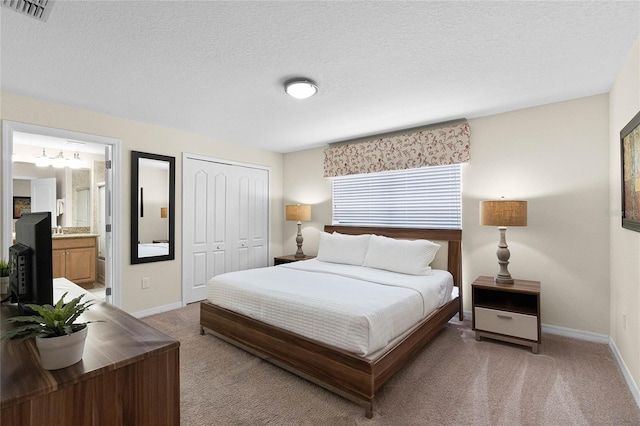 bedroom featuring a closet, connected bathroom, a textured ceiling, and light carpet