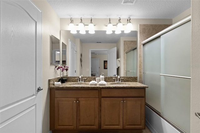 bathroom featuring shower / bath combination with glass door, vanity, and a textured ceiling