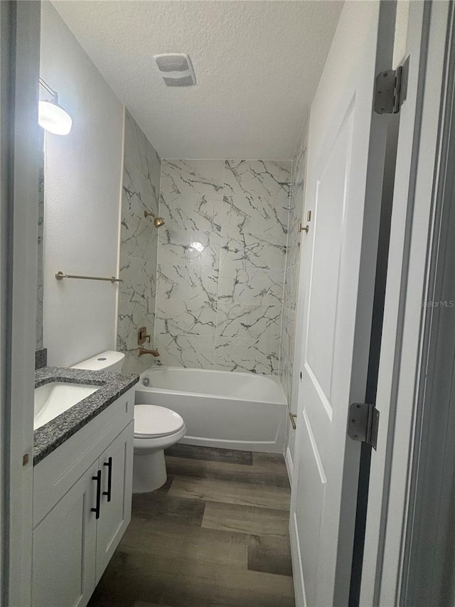 full bathroom featuring a textured ceiling, tiled shower / bath, toilet, wood-type flooring, and vanity