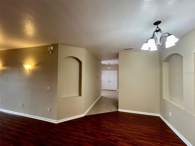 empty room featuring hardwood / wood-style floors, a notable chandelier, and a textured ceiling