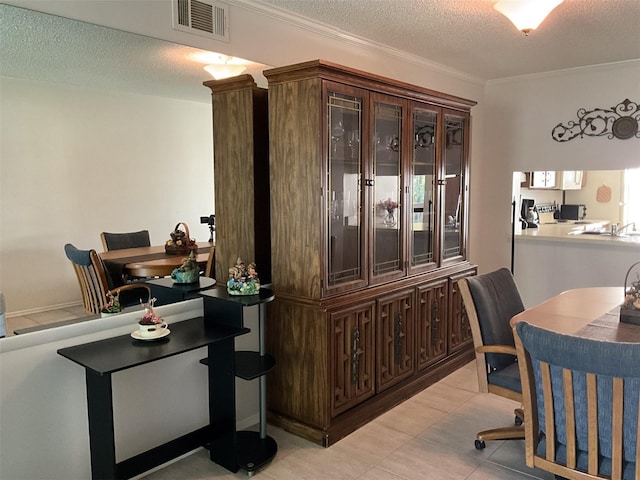 home office with visible vents, a textured ceiling, ornamental molding, and light tile patterned flooring